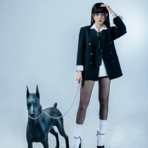 Asian woman in stylish black attire poses with a sleek dog statue in a studio.