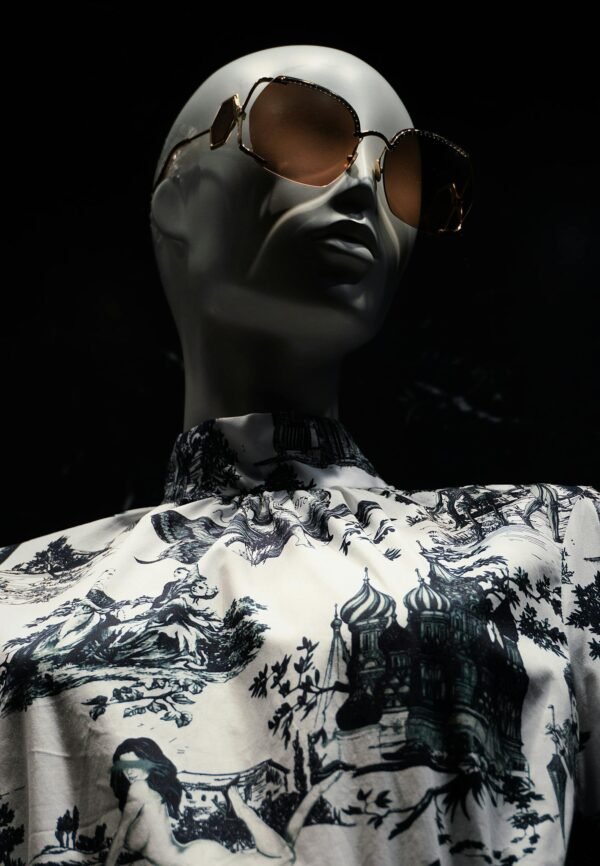 Fashionable mannequin wearing sunglasses and printed shirt on dark background.