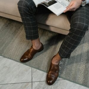 Well-dressed man in brown leather shoes and checkered pants reading a magazine indoors.